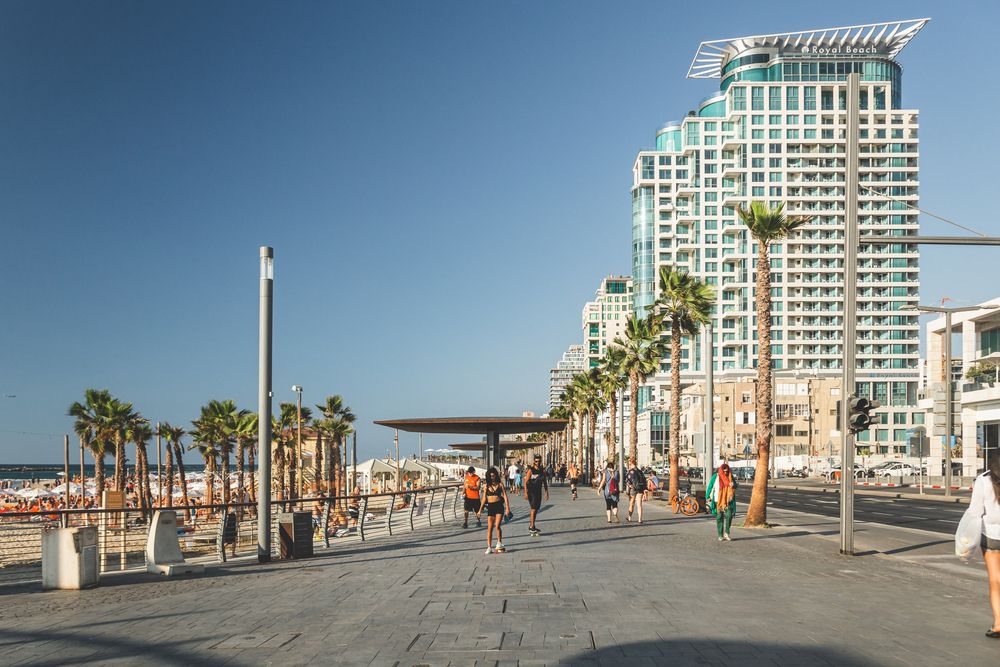 people walking on the promenade in Tel Aviv. Royal Beach Hotel is on the right